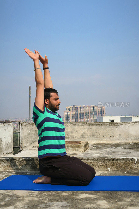 印度男子在屋顶上练习跪着向上行礼(Urdhva Hastasana)瑜伽姿势，德里，印度